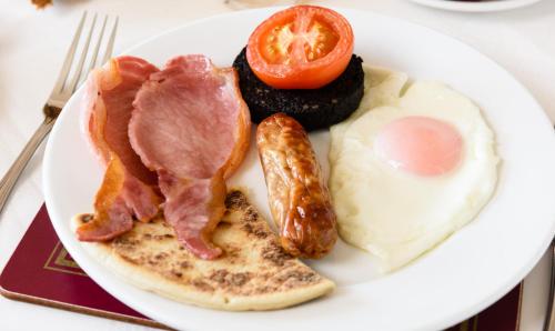 a plate of breakfast food with bacon eggs sausage and tomato at Sunbank House Metro Hotel in Perth