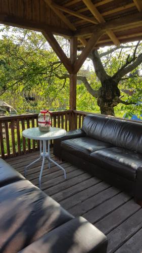a black leather couch on a wooden deck with a table at Édes Otthon Vendégház in Nagybörzsöny