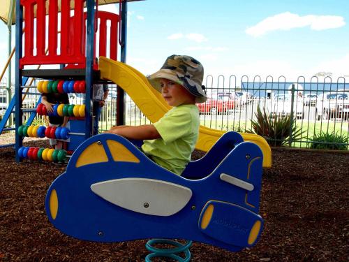 a young boy sitting on a slide in a playground at SkyLodge Temora in Temora
