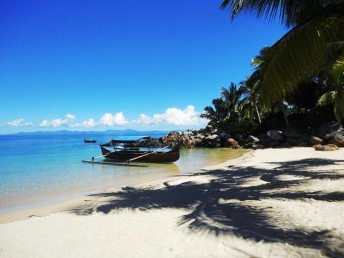a beach with a boat in the water and palm trees at Remo e Berenice in Nosy Komba