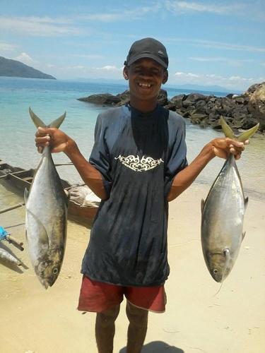 a man holding two fish in his hands on the beach at Remo e Berenice in Nosy Komba