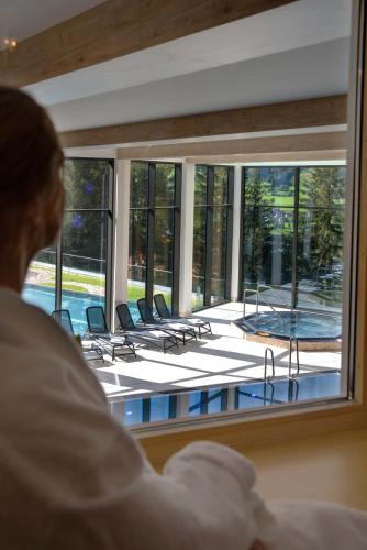 a person looking out of a window at a swimming pool at Hotel Goldried in Matrei in Osttirol