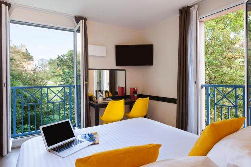 een kamer met een laptop op een tafel en een balkon bij Hôtel Quality Suites Maisons-Laffitte Paris Ouest in Maisons-Laffitte
