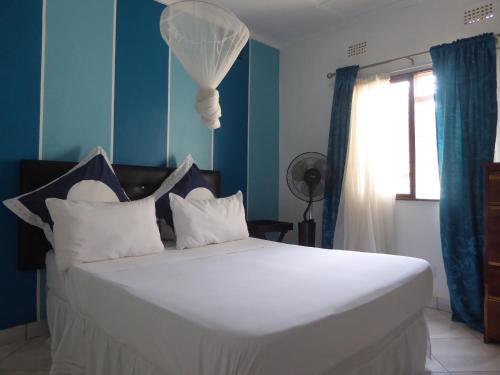 a bedroom with a white bed with blue walls and a window at Natwange Backpackers in Lusaka