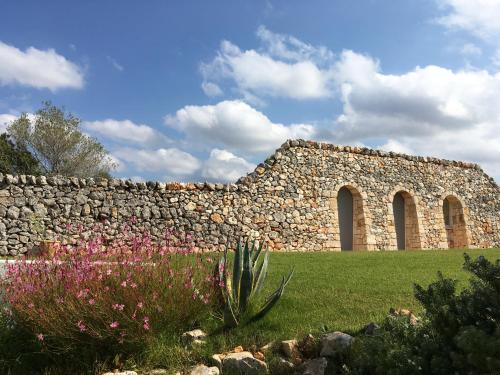 a stone building with a stone wall and flowers at Masserie Maresca in Ostuni