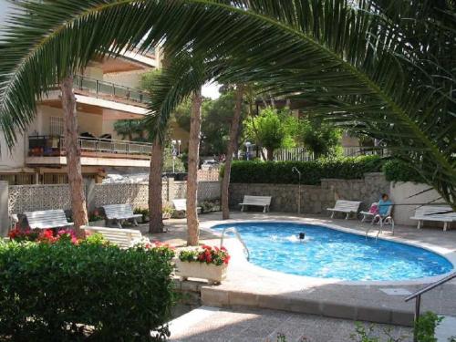 a swimming pool with palm trees and a building at Apartamentos Paradís Palmyra in Salou