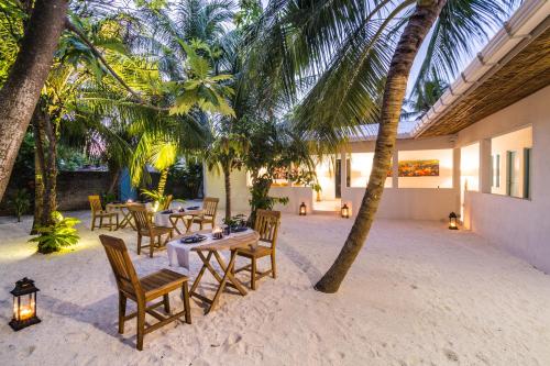a patio with tables and chairs and palm trees at Villa Rosa Maldives in Feridhoo