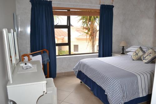 1 dormitorio con 1 cama con cortinas azules y ventana en Swallows Nest, en Stilbaai