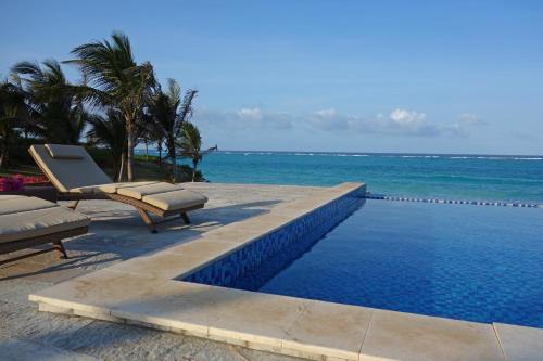 a swimming pool with two lounge chairs and the ocean at Zawadi Hotel, Zanzibar in Michamvi