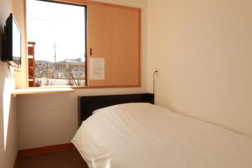 een kleine slaapkamer met een bed en een raam bij Simple Sleep 個室カプセル in Hitoyoshi