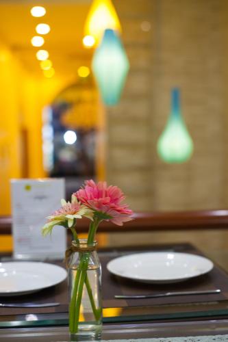 a vase with a flower on a table with plates at Bella Premier Hotel & Rooftop Skybar in Hanoi