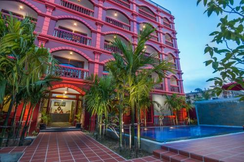 a pink building with palm trees in front of it at Bou Savy Villa in Siem Reap