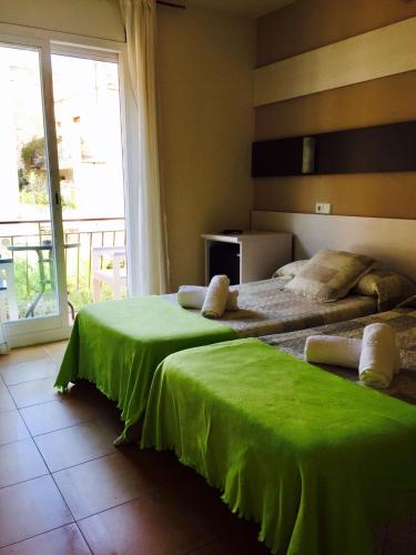 a bedroom with two beds with green sheets and a window at Hostal Termes in Sitges