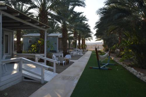 a porch with a hammock and chairs and palm trees at Shkutai Hottub Arava in Ẕofar