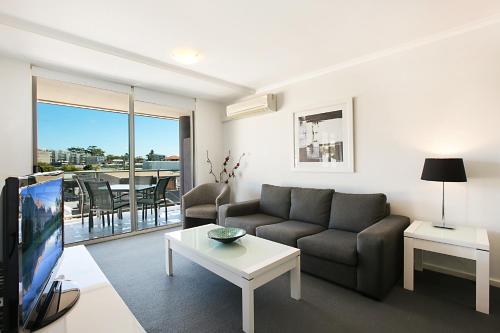 a living room with a couch and a tv and a table at Mantra Nelson Bay in Nelson Bay