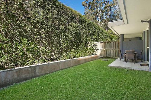 a backyard with a green hedge and two chairs on a lawn at Mantra Nelson Bay in Nelson Bay
