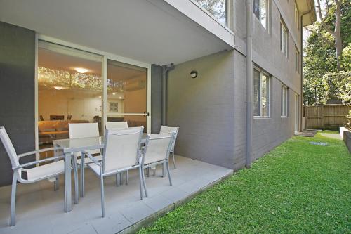 a patio with white chairs and a table and a house at Mantra Nelson Bay in Nelson Bay
