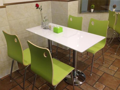 a white table and green chairs in a room at Vatica AnHui Fuyang Linquan South Jiefang Hotel. in Linquan