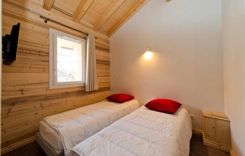 two beds in a room with wooden walls and a window at Odalys Chalet De Marie in Les Menuires