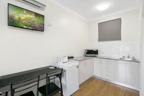 a kitchen with white cabinets and a tv on the wall at Australian Community Villages in Bankstown