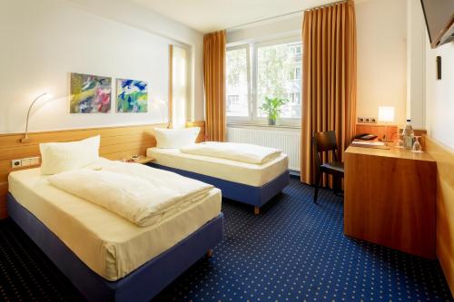 a hotel room with two beds and a desk at MesseHotel Köln-Deutz in Cologne