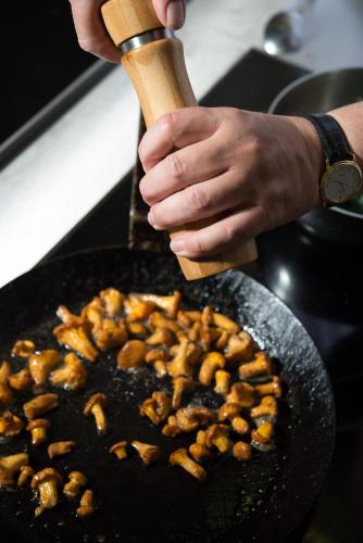 a person holding a wooden spatula cooking food in a pan at Hotel Johannisbad in Bad Aibling