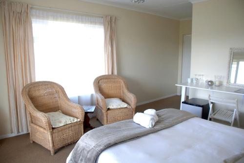 a bedroom with two chairs and a bed and a window at Mandalay Guest House Plettenberg Bay in Plettenberg Bay