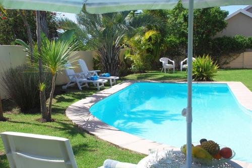 a swimming pool with an umbrella and some chairs at Mandalay Guest House Plettenberg Bay in Plettenberg Bay