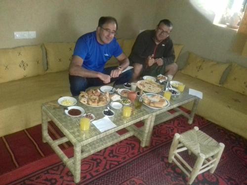two men sitting on a couch with a table of food at Kasbah Izoran in Midelt