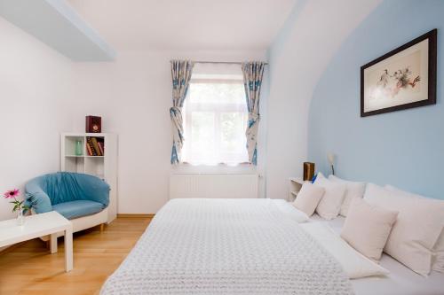 a white bedroom with a bed and a blue chair at Pštrossova Vila - u klášterní zahrady in Bechyně