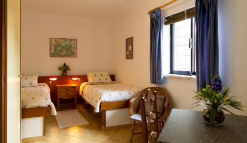 ein Schlafzimmer mit zwei Betten, einem Tisch und einem Fenster in der Unterkunft Markádia in Odivelas