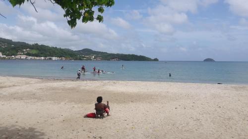 a man sitting on a beach with people in the water at Meryem in La Trinité