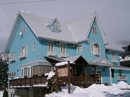 a large blue house with snow on the ground at Pension Come in Minami Uonuma