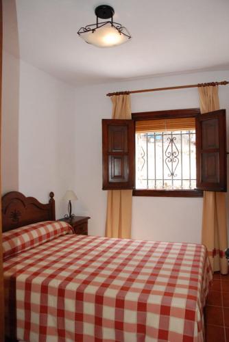a bedroom with a bed with a checkered blanket and a window at alojamiento rural la ermita bubion in Bubión