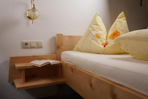 a bed with pillows and a table with a book at Mein Elternhaus Gästehaus Waltraud Fink in Au im Bregenzerwald