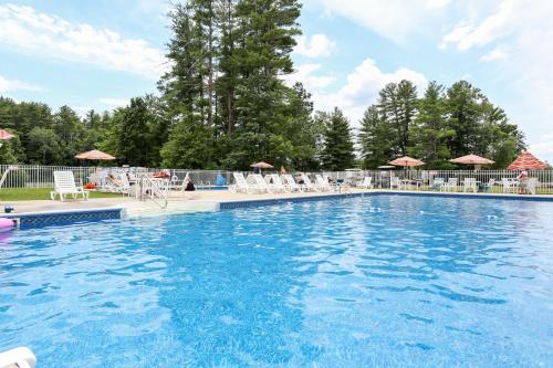 une grande piscine avec des chaises et des parasols dans l'établissement Tuxbury Pond Camping Resort Cottage, à South Hampton