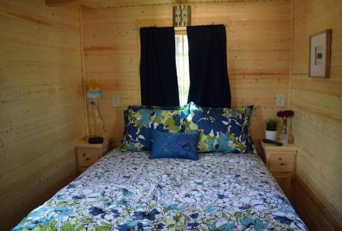 a bedroom with a bed with blue pillows and a window at Tuxbury Pond Camping Resort Tiny House Clara in South Hampton