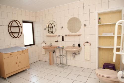 a white tiled bathroom with a sink and a toilet at Ferienhaus am Maibüsch - rollstuhlgerecht in Ulmen