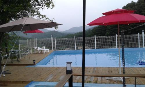 a pool with two umbrellas and a table and chairs at Bluesky Pension in Pocheon