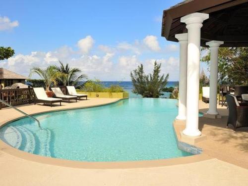 a large swimming pool with chairs and a gazebo at Alexanders Penthouse on the beach in Ocho Rios
