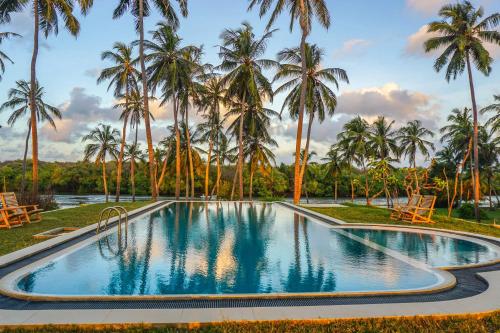 a swimming pool in front of palm trees at Twin Waters Resort in Chilaw