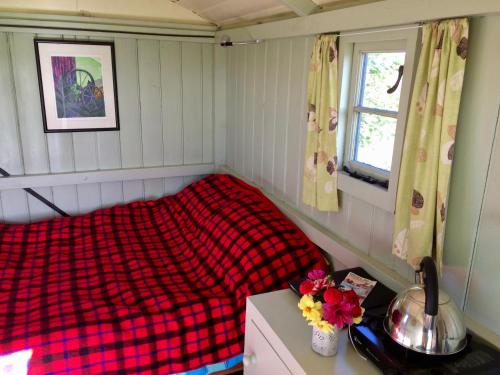 ein Schlafzimmer mit einer roten karierten Decke auf einem Bett in der Unterkunft Shepherd's Hut in Blandford Forum