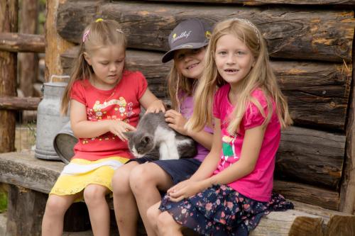 three girls sitting on a bench with a goat at Standlhof in Mariapfarr