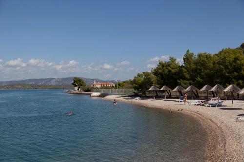 a beach with umbrellas and people swimming in the water at Hotel Stomorin-Marina Hramina in Murter