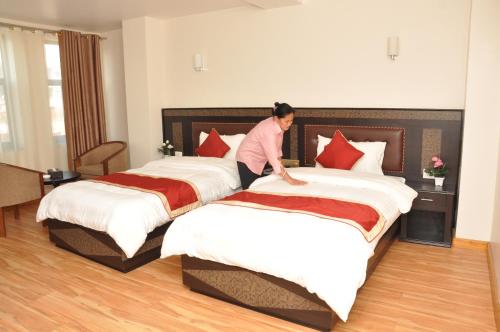 a woman making two beds in a hotel room at Mandala Hotel Kathmandu in Kathmandu