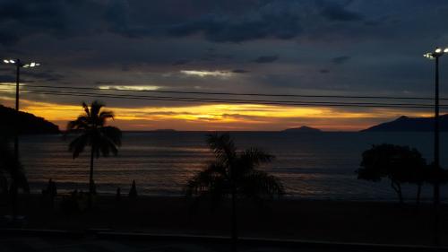 a sunset over the ocean with palm trees on a beach at Apartamento San Martin in Caraguatatuba