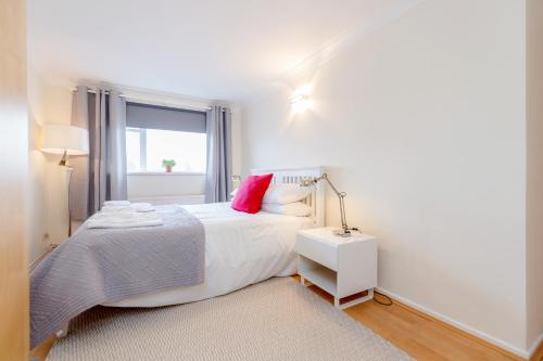 a white bedroom with a bed with a red pillow at Holland Park 2 Bed Flat by BaseToGo in London