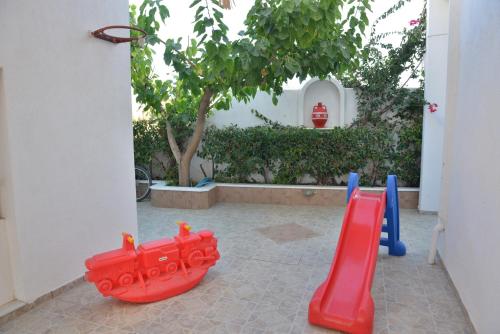 a playground with red and blue slides and a tree at Theoni Studios in Kastraki Naxou