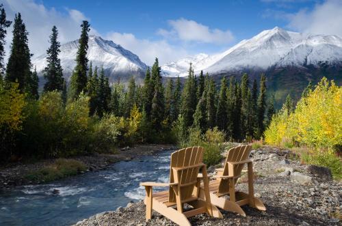 two chairs sitting next to a river with a mountain at McKinley Creekside Cabins in McKinley Park