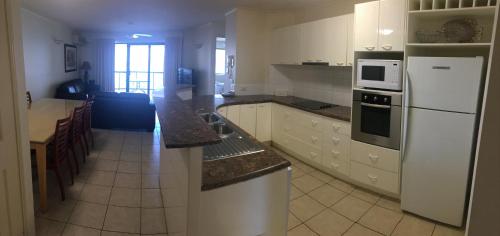 a kitchen with white cabinets and a white refrigerator at Spinnaker Quays in Mooloolaba